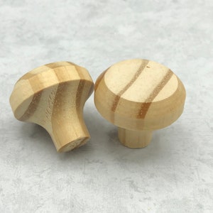 May include: Two wooden drawer knobs with a striped pattern. The knobs are light brown and have a rounded top.