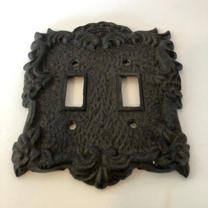 May include: Black cast iron double light switch cover with an ornate design.