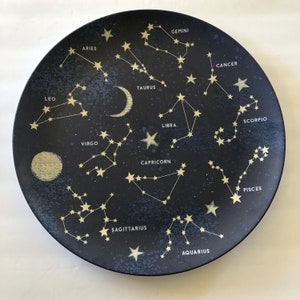 May include: A black plate with a white design of the constellations and their names. The constellations include Aries, Taurus, Gemini, Cancer, Leo, Virgo, Libra, Scorpio, Sagittarius, Capricorn, Aquarius, and Pisces.