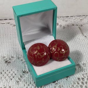 May include: A pair of red and gold round earrings in a teal jewelry box. The earrings have a gold swirl design.