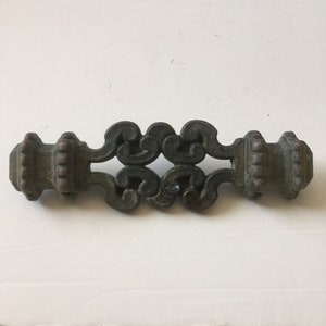 May include: A dark green metal decorative hardware piece with a scroll design and two finials. The piece has a distressed finish and is likely for furniture.