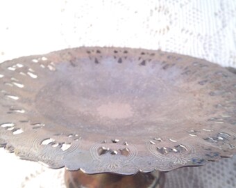 May include: A silver cake stand with a decorative, scalloped edge and a round base. The stand is made of metal and has a shiny finish.