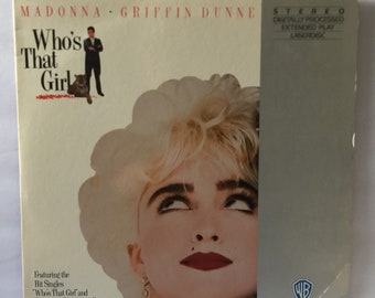 May include: A laserdisc cover featuring a portrait of Madonna with blonde hair and red lipstick. The title of the album is "Who's That Girl" and the album is by Madonna and Griffin Dunne. The Warner Home Video logo is in the bottom right corner.