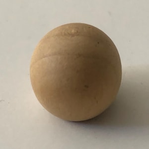 May include: A small, spherical wooden ball with a light brown color. The ball has a smooth surface with visible wood grain and a slight seam. The object is likely a decorative item or a component of a larger craft project.