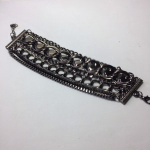 May include: A multi-layered bracelet with a black metal finish. The bracelet features a variety of chain styles and decorative elements, including heart-shaped charms.