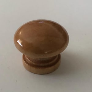 May include: A wooden cabinet knob with a rounded top and a cylindrical base. The knob is a light brown color with a glossy finish. This hardware is suitable for drawers and cabinets.