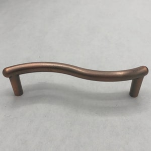 May include: A wavy, copper-colored cabinet pull with rounded ends.