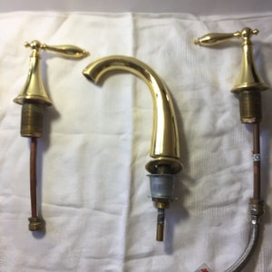 May include: Three gold-toned faucet parts, including a spout, a handle, and a separate handle. The parts are on a white surface.