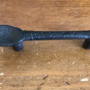 May include: Black cast iron spoon-shaped cabinet door pull with a Y-shaped handle.