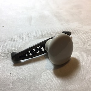 May include: A white ceramic knob with a black metal lever handle. The lever handle has a decorative scroll design.
