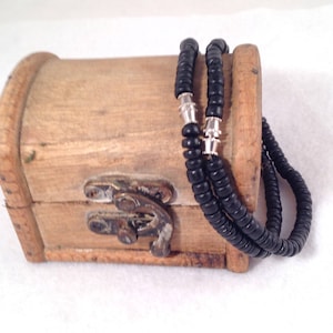 May include: A black beaded necklace with silver accents, resting on a wooden box with a metal latch.