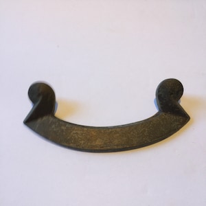 May include: A dark brown metal handle with a curved shape and two rounded ends. The handle has a worn, aged appearance.