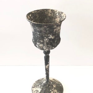 Könnte beinhalten: Ein schwarzer Metallkelch mit einer abgenutzten weißen Oberfläche. Der Kelch hat einen runden Fuß und einen hohen Stiel.