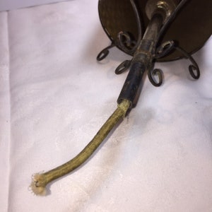 K&ouml;nnte beinhalten: Nahaufnahme eines Vintage-Metall-Lampenschirms mit brauner Oberfl&auml;che und einem gr&uuml;nen Stoffkabel. Der Lampenschirm hat ein dekoratives Metalldesign und ist an einem Metallkabel befestigt.
