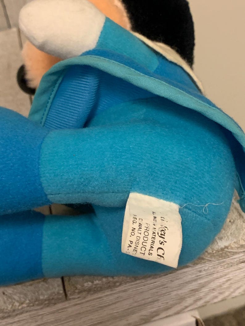 May include: A plush toy in shades of blue, with a white and black head. The toy has a tag that reads "Gey's CF PRODUCT" and "WALT DISNEY". The toy is made of soft material.