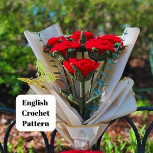 Puede incluir: Un ramo de rosas rojas de ganchillo envuelto en papel beige con hojas verdes y una mariposa amarilla. El ramo está sentado en una valla de metal negro. El texto "English Crochet Pattern" está en un rectángulo blanco.