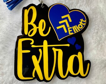 May include: A black and yellow keychain with the text "Be Extra" and a blue heart with the text "Elliott" on it. The keychain has a blue tassel.