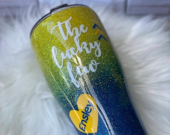 May include: A yellow and blue glitter tumbler with the text "The lucky few" and a heart with the name "Ensley" on it.
