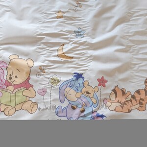 May include: A white fabric with a Winnie the Pooh theme. The fabric features Winnie the Pooh, Piglet, Tigger, and Eeyore. The characters are surrounded by stars, a crescent moon, and flowers.