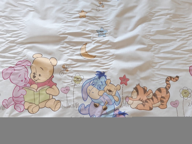 May include: A white fabric with a Winnie the Pooh theme. The fabric features Winnie the Pooh, Piglet, Tigger, and Eeyore. The characters are surrounded by stars, a crescent moon, and flowers.