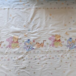 May include: White fabric featuring a repeating pattern of Winnie the Pooh and his friends. The characters are depicted in a cartoon style and are surrounded by stars and flowers. The fabric is suitable for crafting projects, such as quilts, blankets, and cushions.