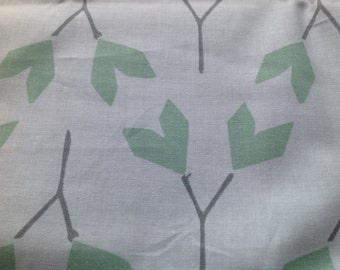 Op de afbeelding: Witte stof met een herhalend patroon van groene bladeren en grijze stelen. De bladeren zijn gestileerd en lijken op pijlen.
