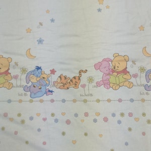 May include: A light blue fabric with a Winnie the Pooh theme. The fabric features Winnie the Pooh, Piglet, Tigger, and Eeyore characters. The fabric also has a pattern of stars, hearts, and flowers.