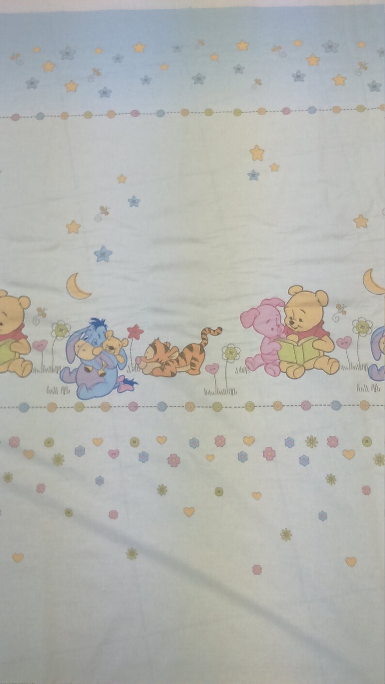 May include: A light blue fabric with a Winnie the Pooh theme. The fabric features Winnie the Pooh, Piglet, Tigger, and Eeyore characters. The fabric also has a pattern of stars, hearts, and flowers.