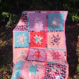 May include: A pink and blue patchwork quilt with a star design. The quilt is made of different fabrics with various patterns, including polka dots, stripes, and floral prints.