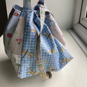 Peut inclure: Un sac à cordon en vichy bleu et blanc avec un imprimé floral et un motif de libellule. Le sac a une longue sangle et est fait de tissu.