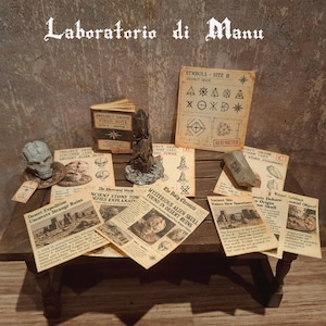 May include: A collection of miniature props including a small book titled Project Orion Field Note, a grey alien skull figurine, a stone-like tower, a stone fragment, and several printed papers with headlines like Mysterious Alien Skull Found in Desert Ruins.