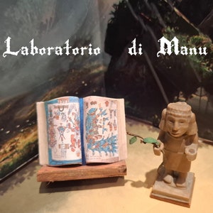 May include: An open book with colourful illustrations and a blue ribbon bookmark. The book is on a wooden stand. A small, brown figurine of a person with a branch in one hand is standing on a small, brown base.