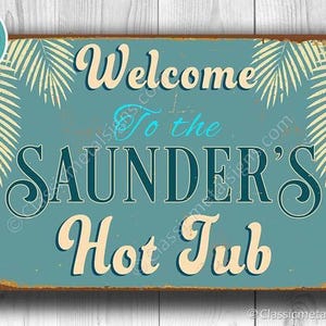 May include: A rectangular metal sign with a teal background and distressed brown edges. It features cream-coloured palm leaf illustrations in the corners and the text "Welcome To the SAUNDER'S Hot Tub" in a mix of cream and light blue script and serif fonts.