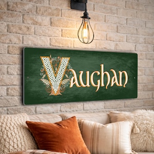 May include: A rectangular green metal sign with the name "Vaughan" in an elegant font. The letter "V" is decorated with a Celtic knot design. The sign is mounted on a brick wall above a sofa with decorative pillows.