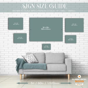 a cozy living room with a gray sofa and a brick wall backdrop. The sofa is positioned in front of a wall with a guide for sign size, providing dimensions for various sign sizes.