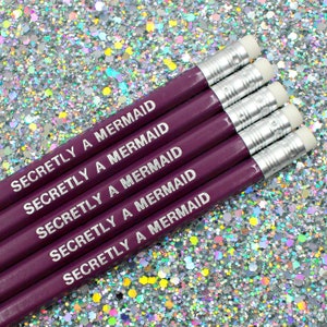 May include: Five purple pencils with silver accents and white erasers. Each pencil is engraved with the text "Secretly a Mermaid".