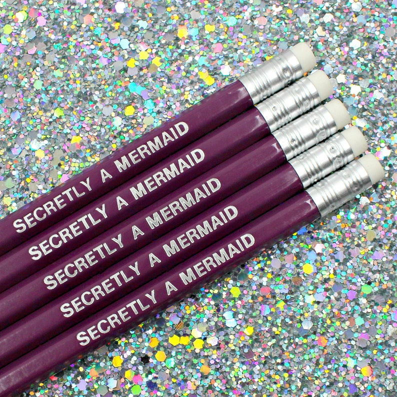 May include: Five purple pencils with silver accents and white erasers. Each pencil is engraved with the text "Secretly a Mermaid".