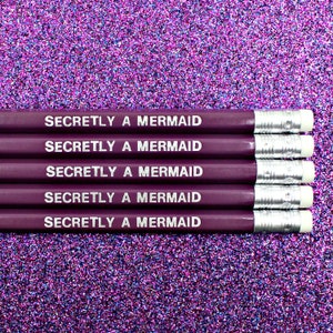 May include: Five purple pencils with silver accents and white erasers. Each pencil has the text "Secretly a Mermaid" printed on it in white.