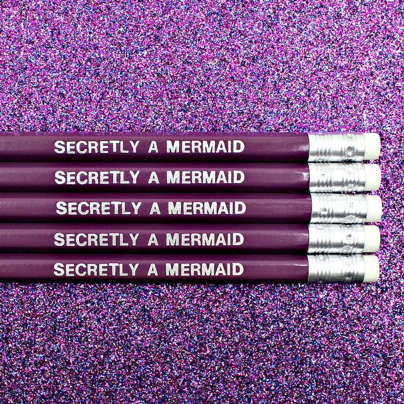 May include: Five purple pencils with silver accents and white erasers. Each pencil has the text "Secretly a Mermaid" printed on it in white.