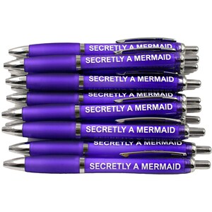 May include: A stack of ten purple pens with silver accents. Each pen has the text "Secretly a Mermaid" printed in white on the barrel.