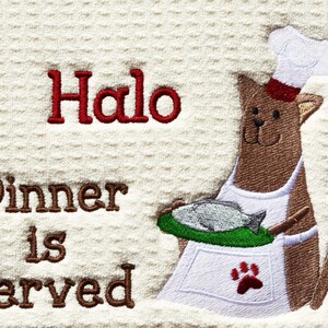 May include: A brown cat wearing a white chef's hat and apron holds a plate with a fish on it. The text "Halo Dinner is Served" is embroidered on the white background.