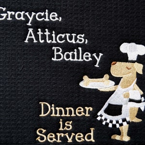 May include: Black doormat with white embroidered text that reads "Graycie, Atticus, Bailey Dinner is Served". A cartoon dog wearing a chef's hat and apron is holding a plate with a bone on it.