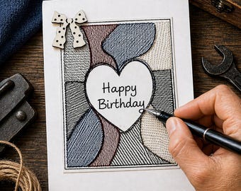 May include: A birthday card with a stitched design in blue, burgundy, and beige. The card features a white heart with the words "Happy Birthday". A wooden bow with polka dots is attached to the top left corner.