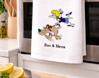 May include: White kitchen towel featuring an embroidered cartoon of a dog and a person running. The dog is brown with a green nose and the person is wearing blue and yellow. The text "Roo & Neve" is below the image.