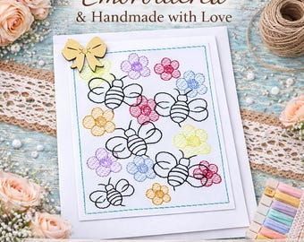 May include: A white greeting card featuring an embroidered design of black-outlined bees and colourful flowers in yellow, red, blue, and purple. A small gold-coloured wooden bow is attached to the top left corner of the card, which is centred on a white base.