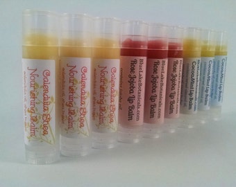 May include: A row of eight lip balm tubes with different flavors, including Calendula Shea, Rose Jojoba, and Cocoa Mint. The tubes are clear and show the lip balm inside.