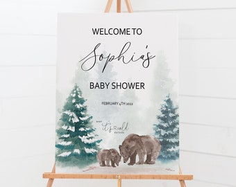May include: A baby shower welcome sign on an easel. The sign features the text "Welcome to Sophia's Baby Shower" with watercolor illustrations of pine trees and bears. The date "February 4th 2022" is also displayed.