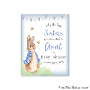 Puede incluir: Una impresi&oacute;n para baby shower con una ilustraci&oacute;n en acuarela de un conejo con una chaqueta azul. El texto dice "solo las mejores hermanas son promovidas a t&iacute;a", con el nombre del beb&eacute; y la fecha de llegada.