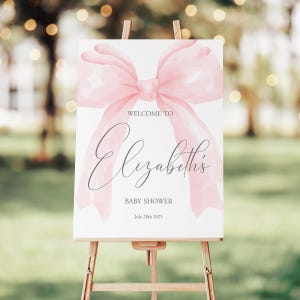 May include: A white welcome sign with a pink watercolor bow and the text "Welcome to Elizabeth's Baby Shower July 28th 2023".