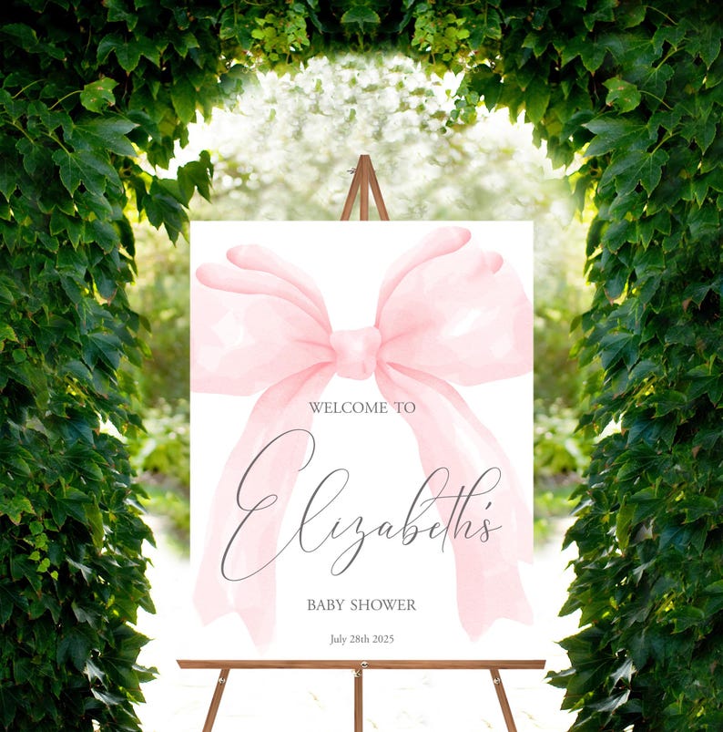May include: A white welcome sign with a large pink watercolor bow. The text reads "Welcome to Elizabeth's Baby Shower July 28th 2025".